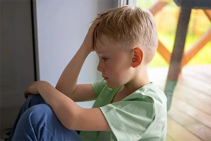 imagem de uma criança loira, de camisa verde, aparentemente deprimida