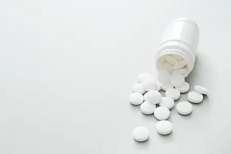 um pote de comprimidos aberto, sobre uma superfície, com vários comprimidos caindo para fora