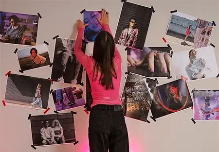imagem de uma mulher colando uma foto na parede, coberta de fotos de uma pessoa ou casal