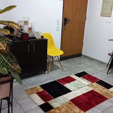 imagem da recepção, com uma cadeira amarela ao lado da uma mesa de café, com um tapete quadriculado no centro e um vaso de planta no canto