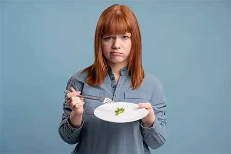 uma mulher ruiva, de camisa de manga comprida azul, segurando um prato com pouca comida