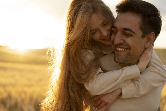 imagem de um casal heteroafetivo abraçado e sorridente, com o por do sol ao fundo