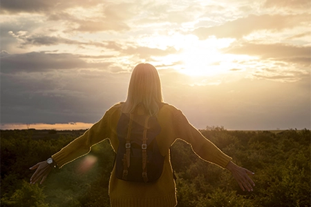 uma mulher olhando para o por do sol em um campo vasto