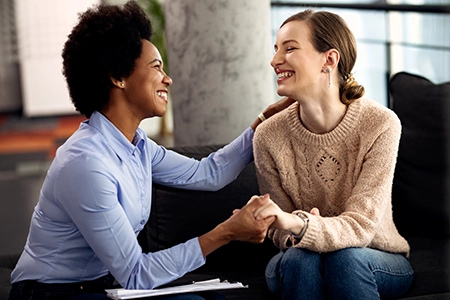 duas mulheres, sentadas, de mãos dadas, sorrindo