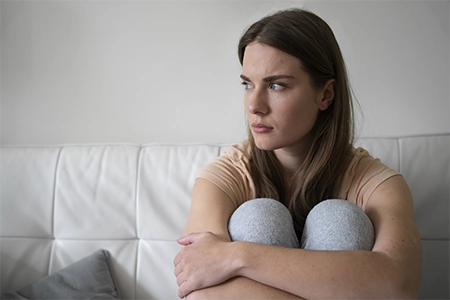 uma mulher, abraçada aos joelhos, com ar de tristeza